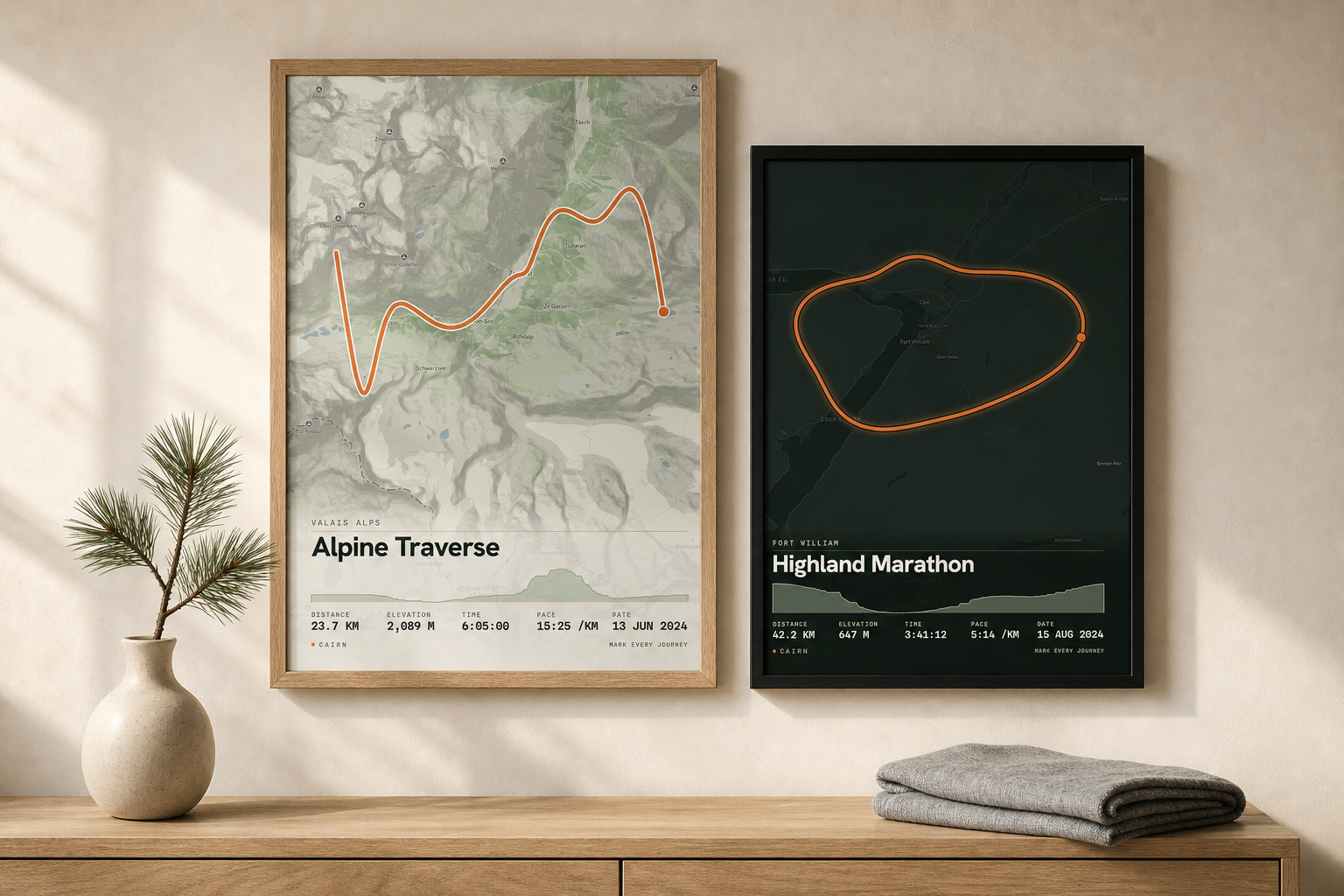 Two framed map-art prints of real routes on a warm wall, above an oak console with a pine sprig and folded textile